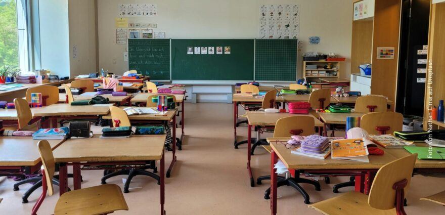 Ein leeres Klassenzimmer, aber mit vielen bunten Federtaschen und Heften auf den Schultischen.